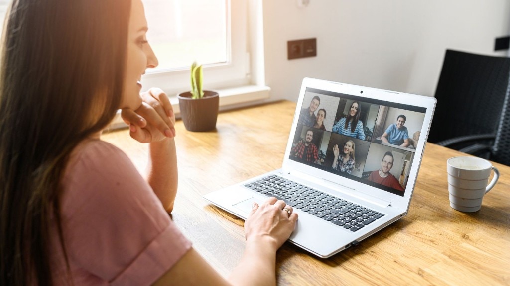 Woman at a home desk engaged in a video call with five participants on her laptop